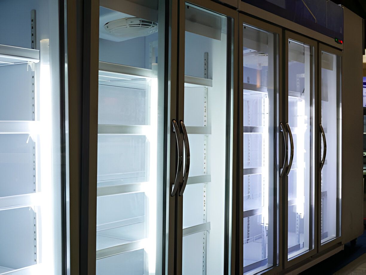 Empty glass-door refrigerators with interior lights on, in a commercial setting.