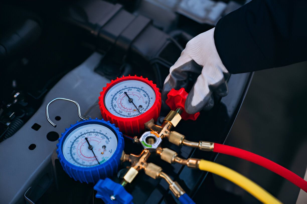 Gloved hand adjusting gauges connected to a car's AC system with red, yellow, and blue hoses.