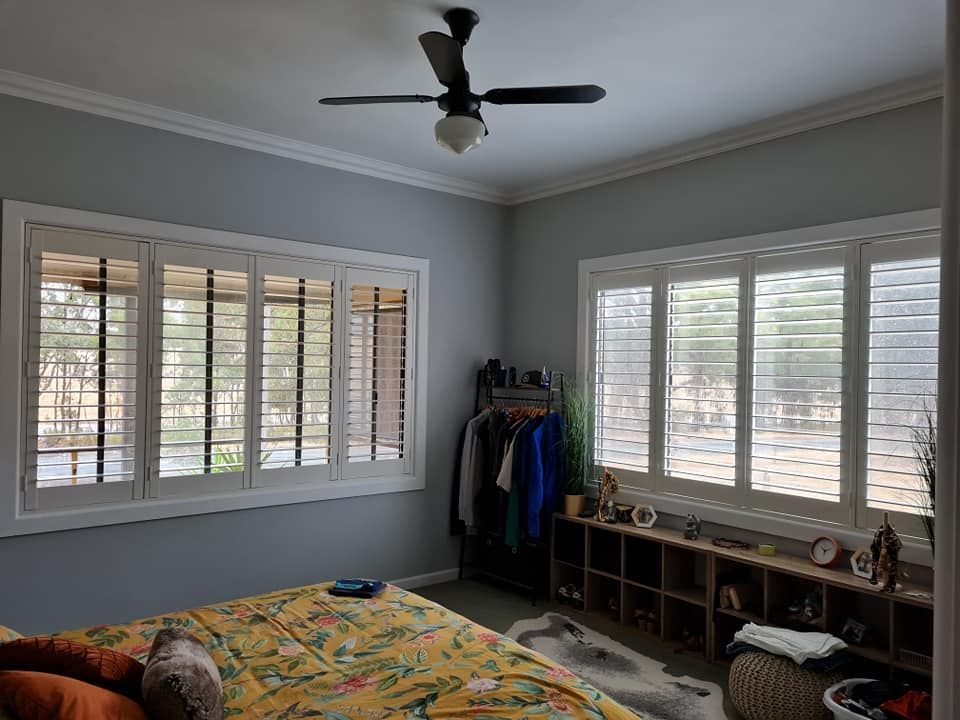 Bedroom with gray walls, white shutters, ceiling fan, bed, and a wooden cubby shelf.