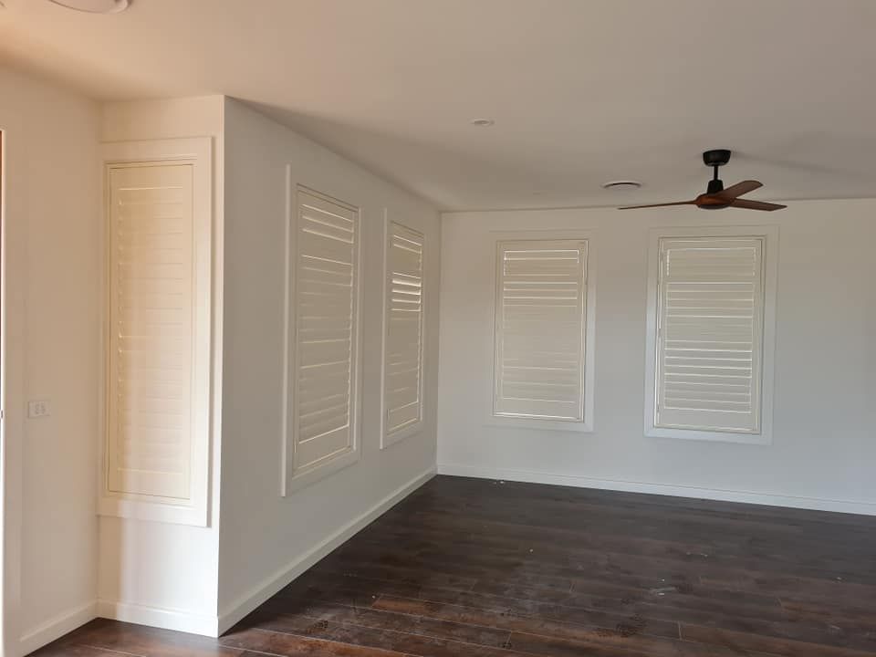 Empty room with three window shutters, ceiling fan, and dark wooden floor.