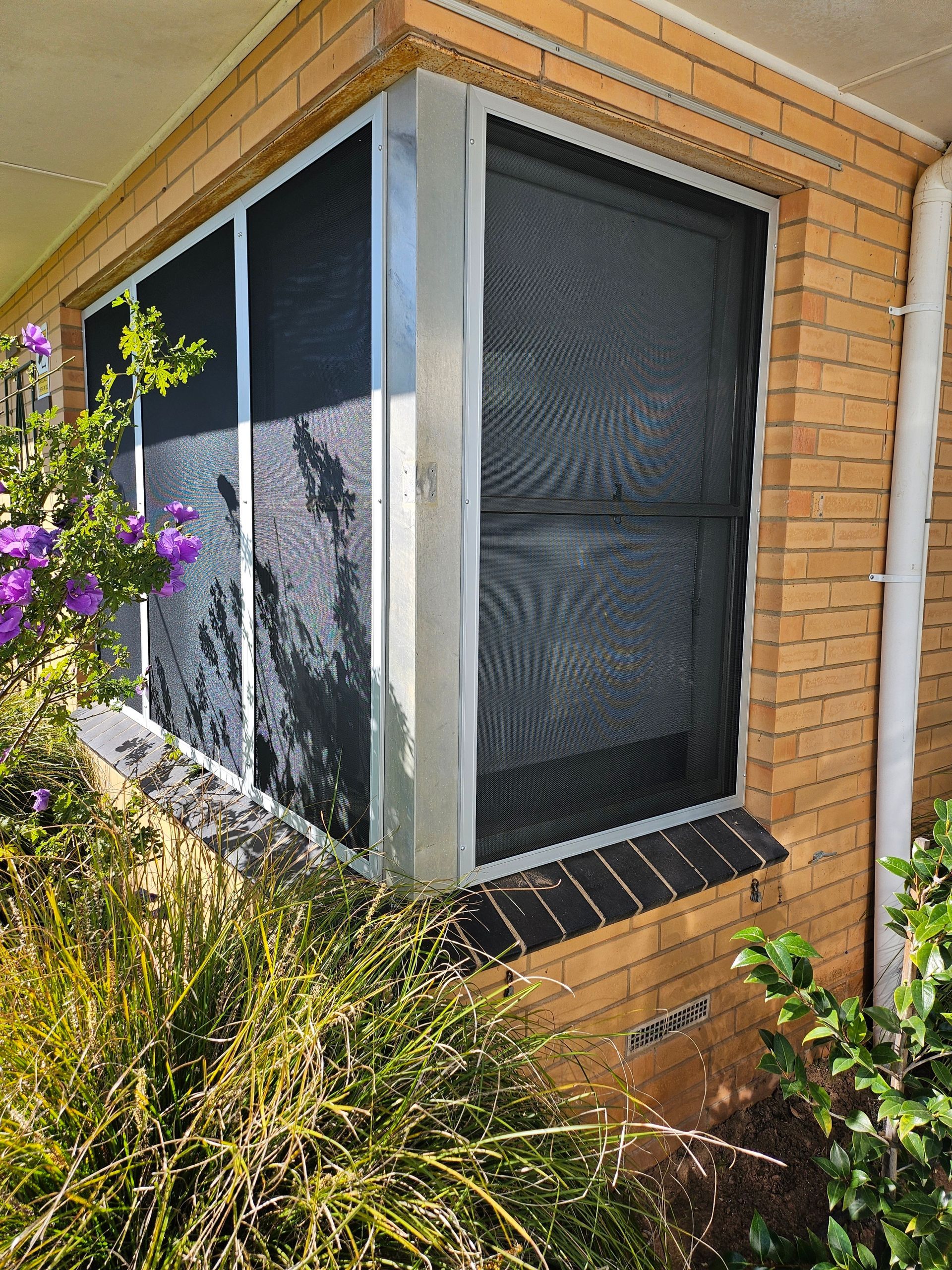 View through a screen window of a white van parked in front of a house.