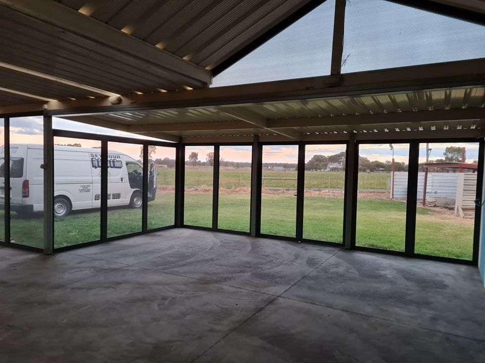 Interior view of a sunroom with glass windows overlooking a field. A white van is visible.
