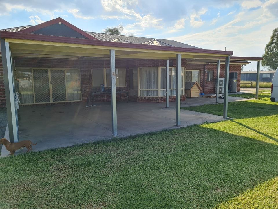 A house with a covered patio, concrete floor, and green lawn. Brown dog walks on the lawn.
