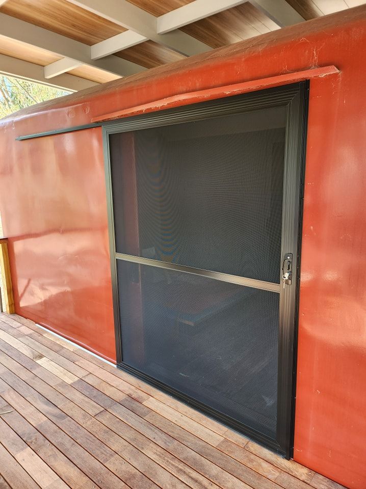 Sliding screen door, black frame, closed on red building exterior, wooden deck.