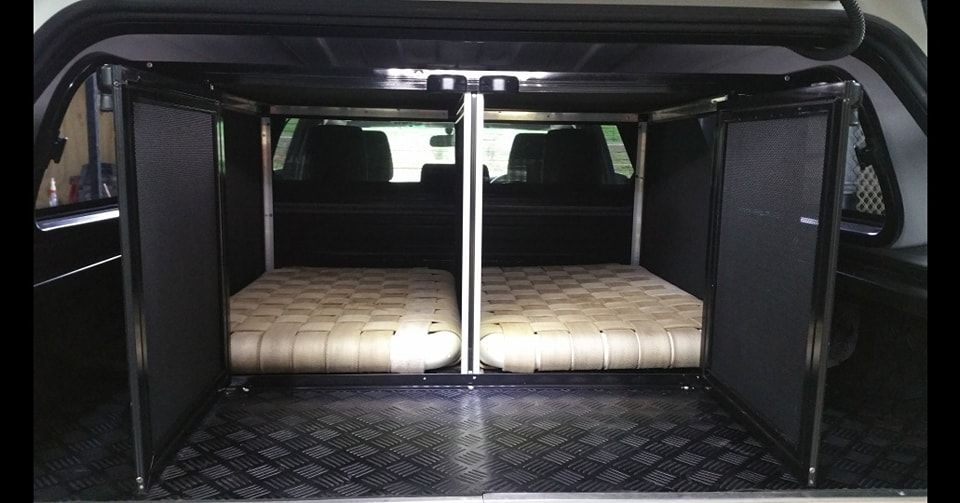 Dog kennels built inside a truck bed, featuring two beds and separate entry doors.