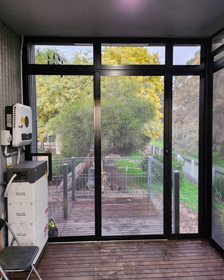 Solar power equipment inside a room with large window. A view of green trees and wooden decking is visible.