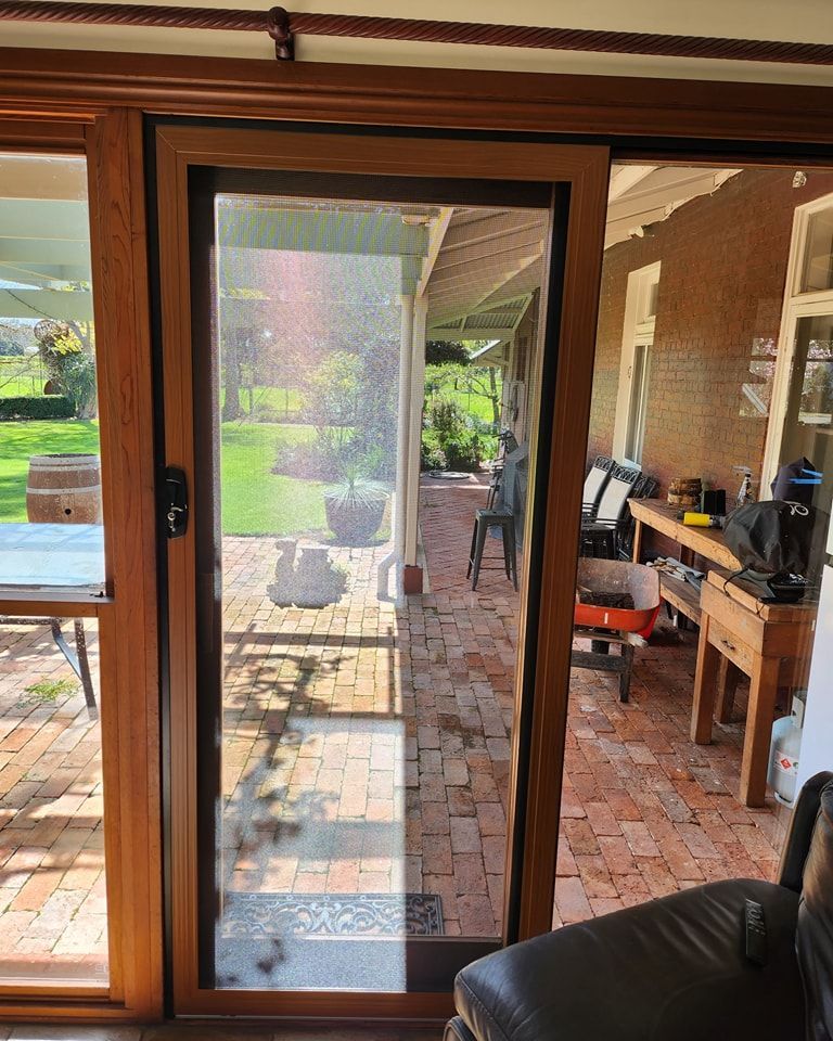 Sliding glass door with screen open to brick patio, lawn, and outdoor furnishings.