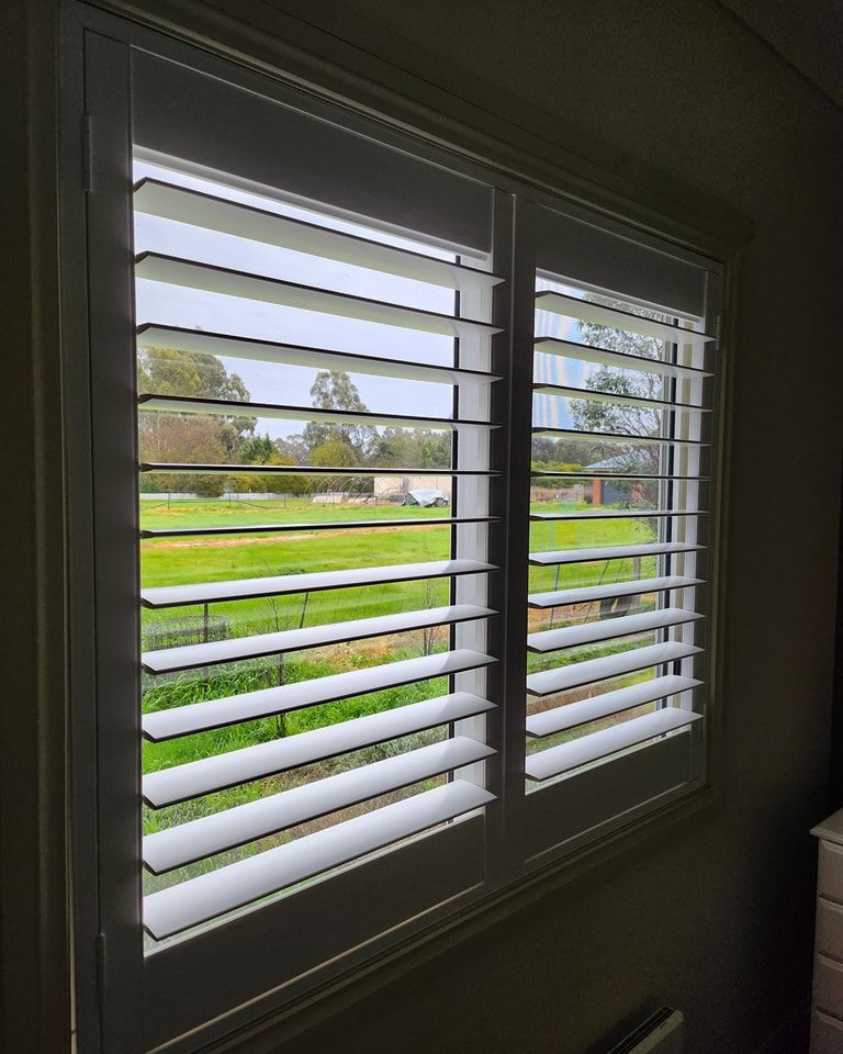 White shuttered window looking out to green landscape.