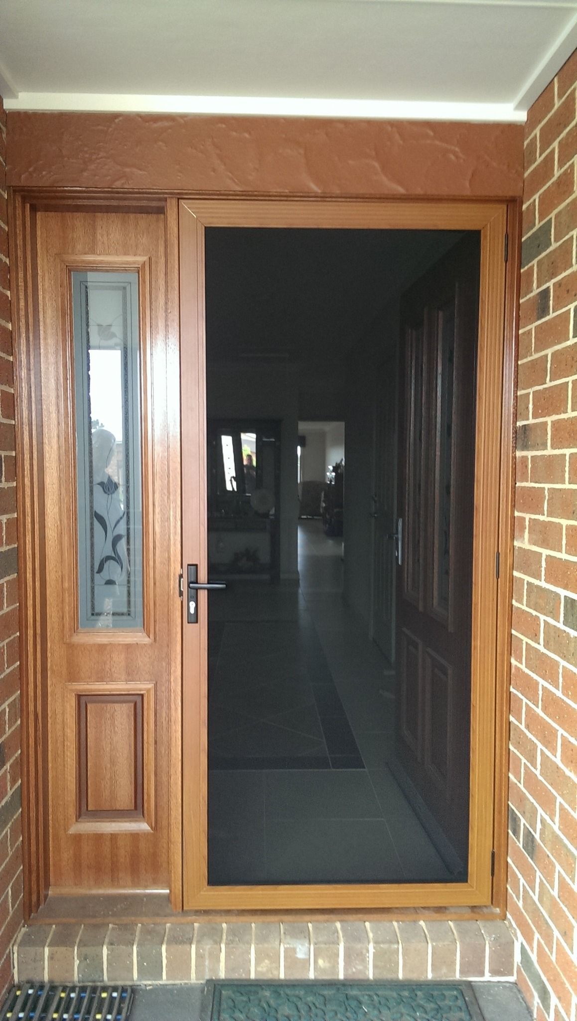 Wooden front door with screen door open, leading into a house with a brick exterior.