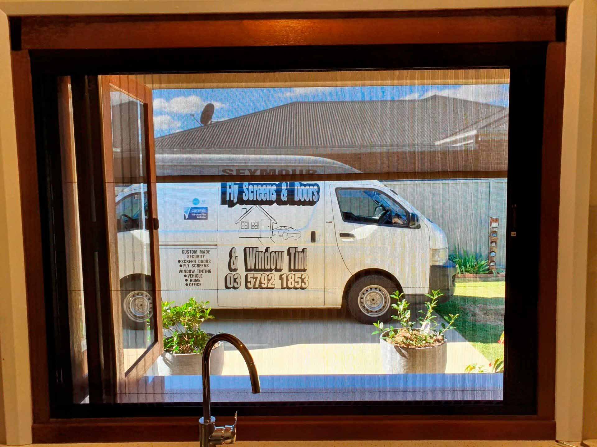View through a screen window of a white van parked in front of a house.