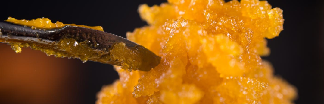 Close-up of an orange, grainy hash substance being scooped with a small silver spoon device