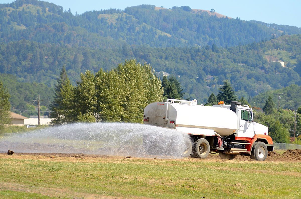 A tanker truck is spraying water on a field with mountains in the background