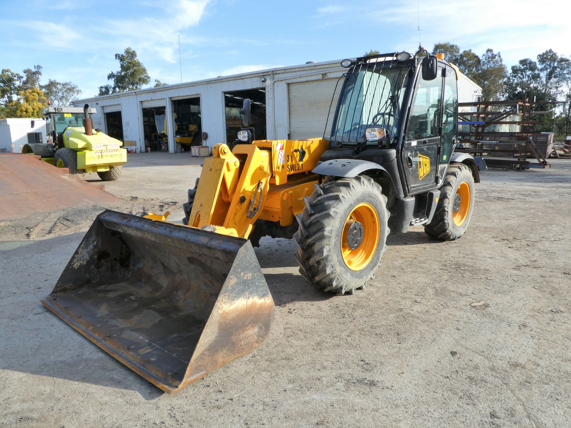 A yellow tractor with a large bucket is parked in front of a building.