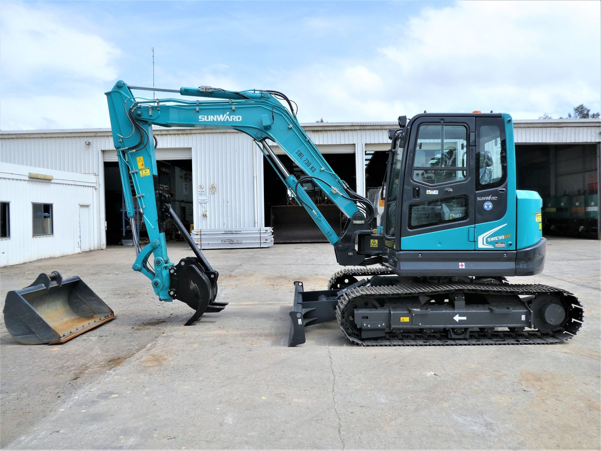 A blue excavator is parked in a parking lot in front of a building.