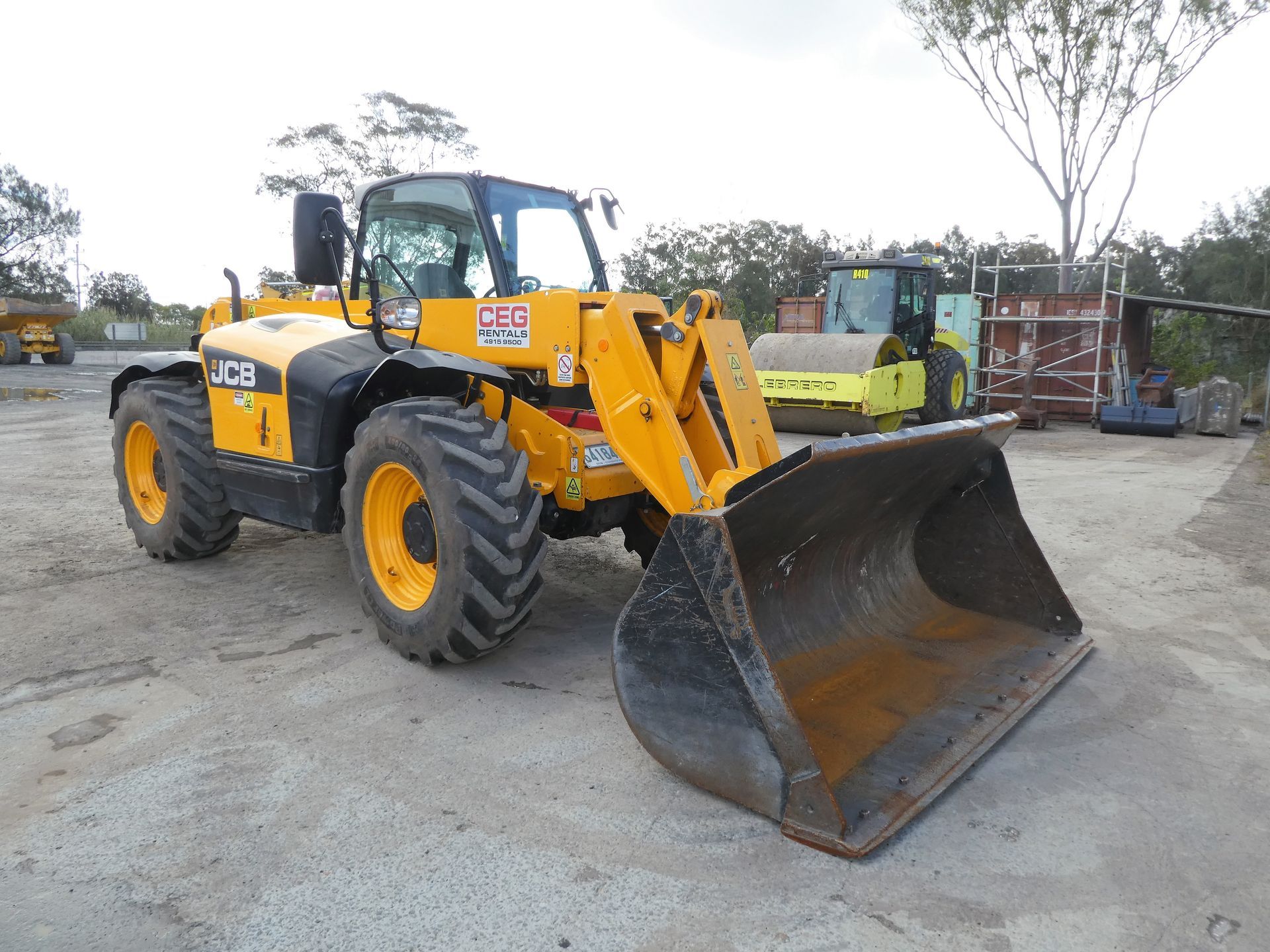 A yellow tractor with a large bucket is parked in a dirt lot.