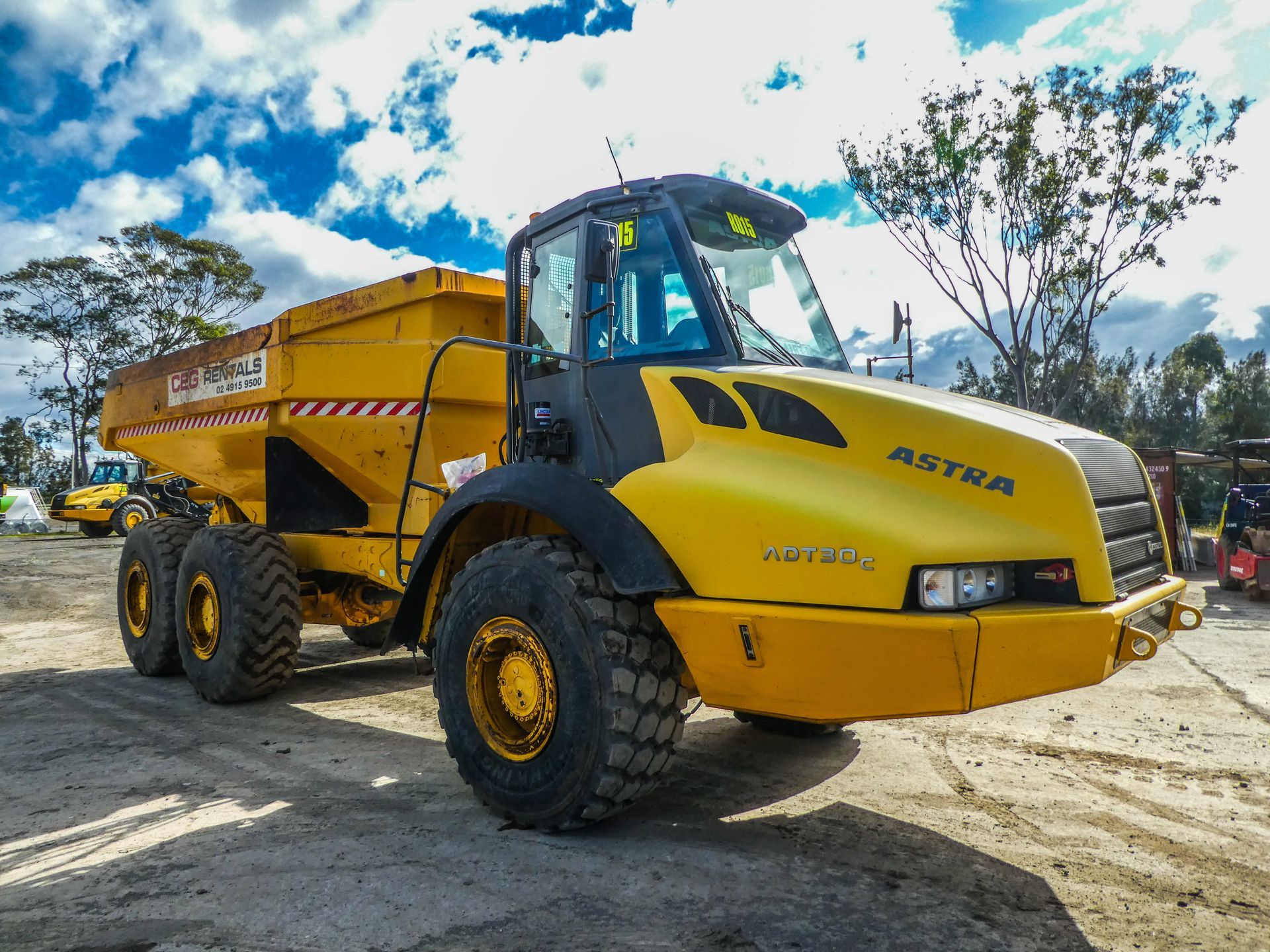 A yellow dump truck is parked in a dirt lot.