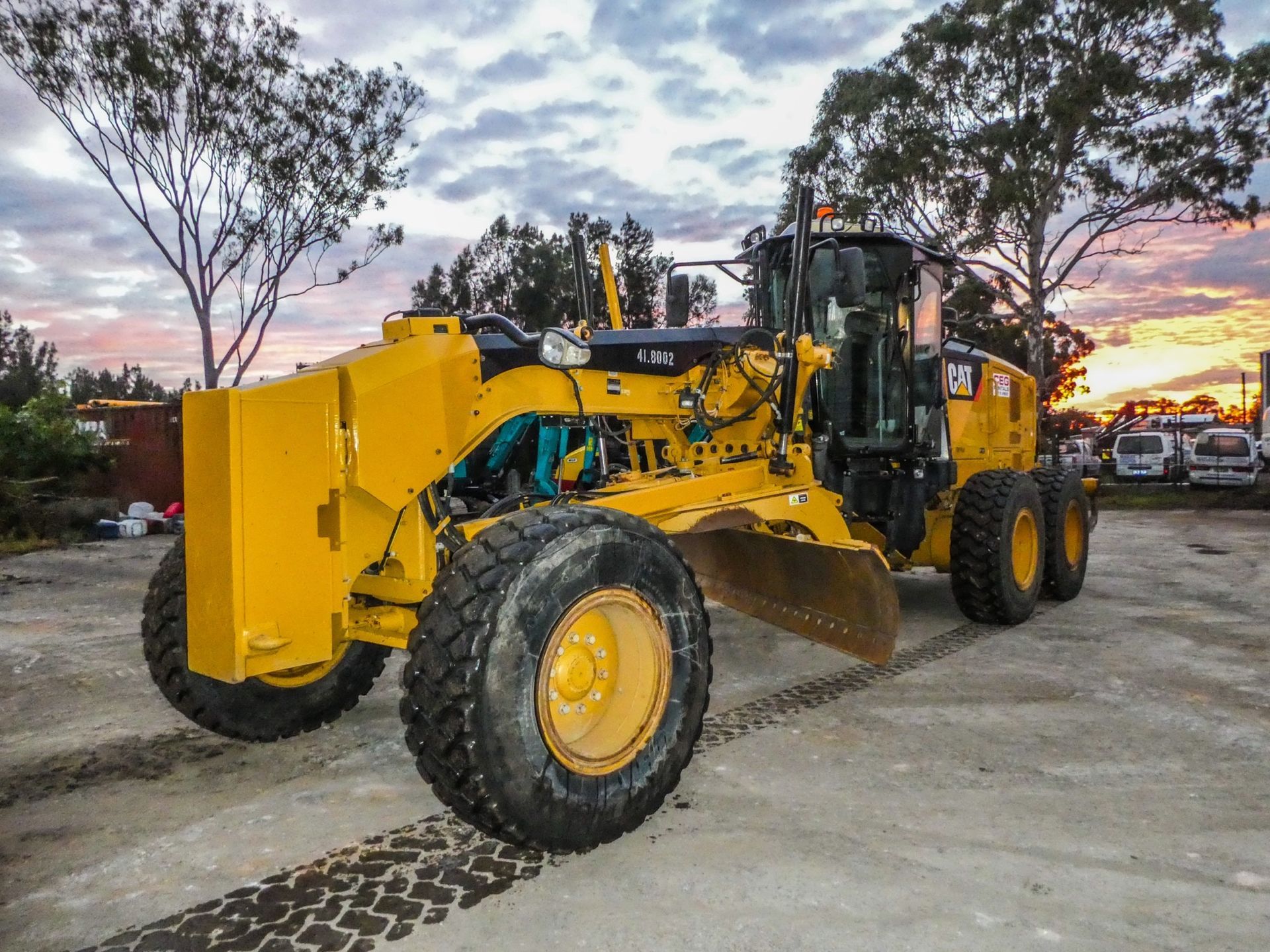 A yellow tractor is parked in a parking lot at sunset.