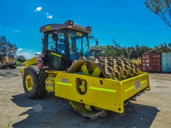A yellow and black tractor is parked in a dirt lot.