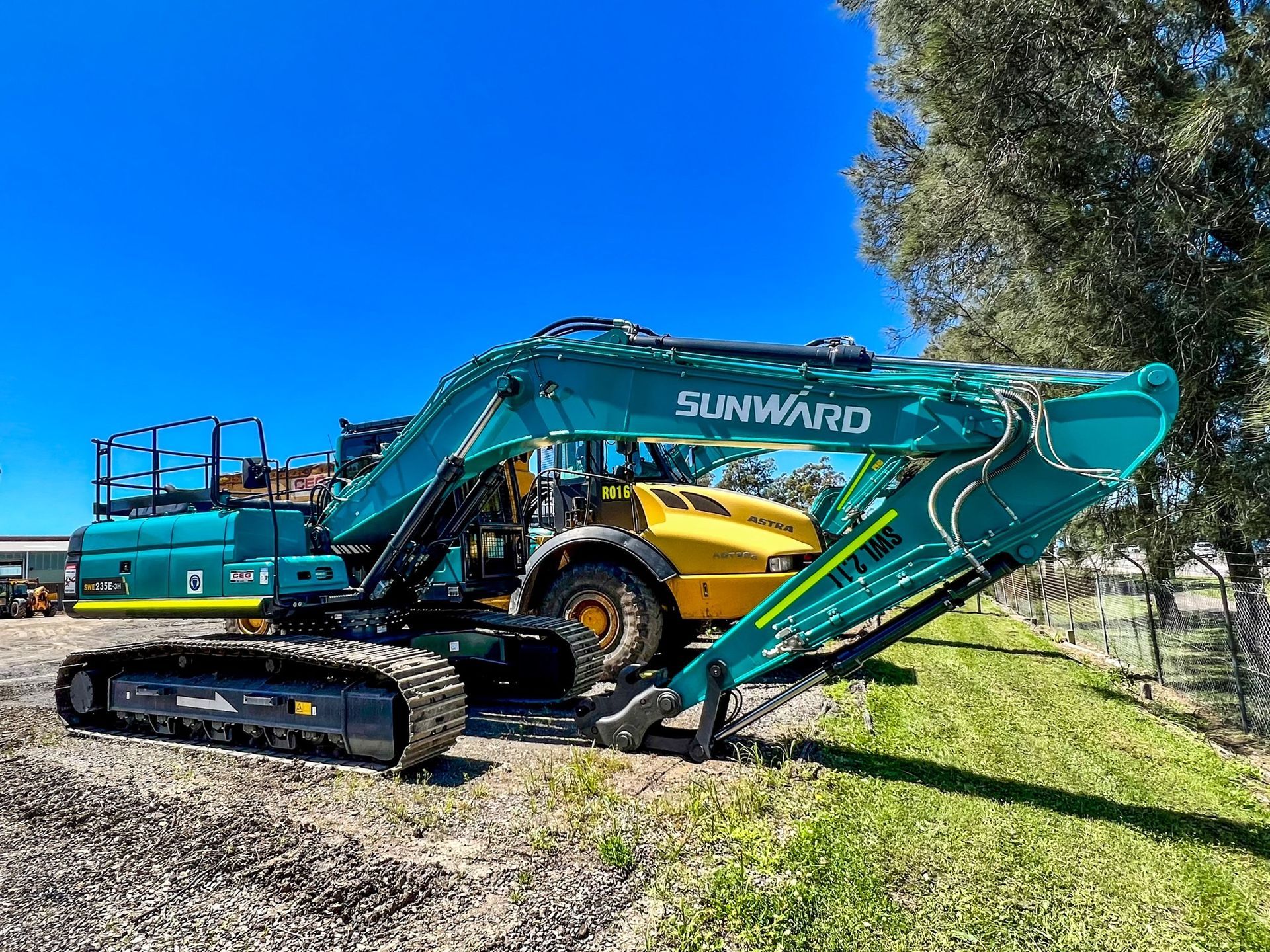 A green and yellow excavator is parked in a grassy field.