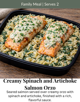 Two salmon fillets topped with creamy sauce served over creamy spinach and artichoke orzo in a black container.