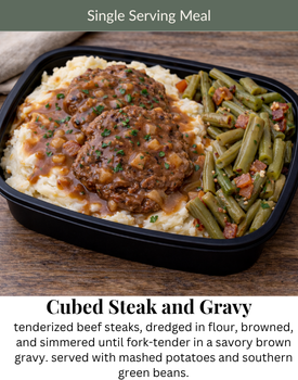 A single-serving meal of cubed steak with brown gravy, mashed potatoes, and green beans in a black container.