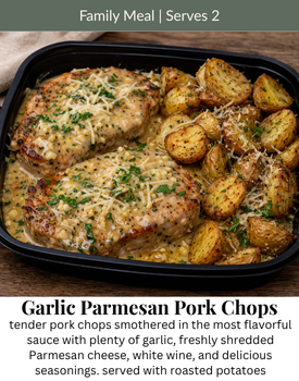 A black container holds two garlic parmesan pork chops in a creamy sauce next to a side of golden roasted potatoes.