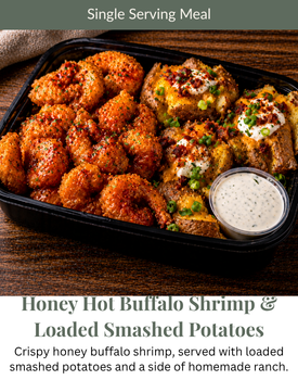 A meal container of honey hot buffalo shrimp, loaded smashed potatoes, and a side of ranch dressing on a wooden table.