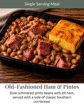 A single serving of slow-simmered pinto beans with pit ham and a piece of cornbread in a black container.