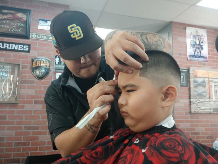 A boy is getting his hair cut by a barber wearing a san diego padres hat