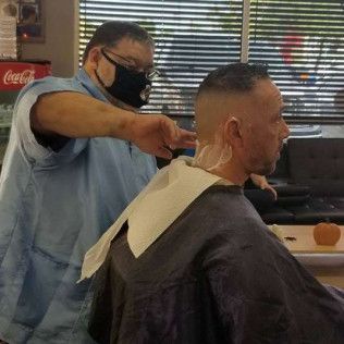 A man is getting his hair cut by a barber wearing a mask.