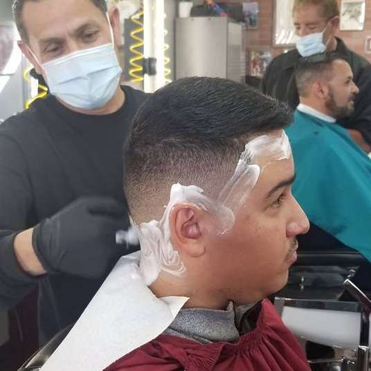 A man is getting his hair cut by a barber wearing a mask.