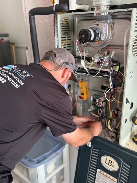 HVAC technician working on a furnace, wires visible. Gray hat, black shirt. Inside a building.