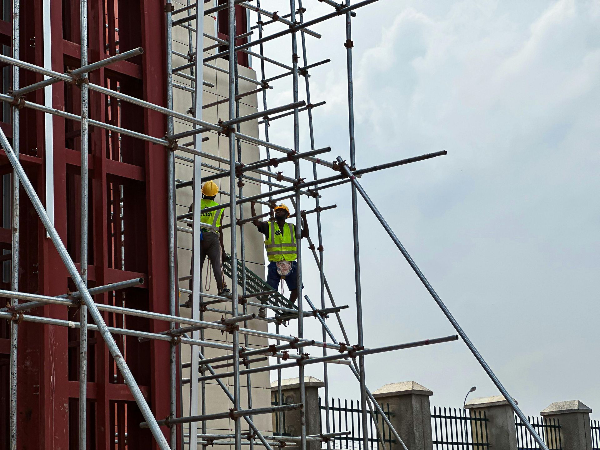 Two construction workers on scaffolding next to a building; they wear hard hats and safety vests.