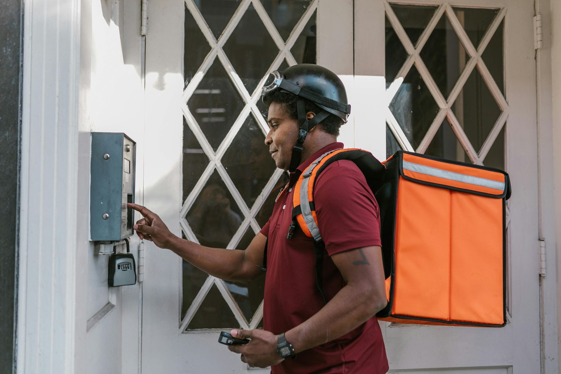 A delivery man with a backpack is ringing a doorbell.