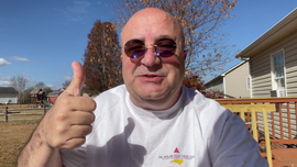 A bald man wearing sunglasses is giving a thumbs up.