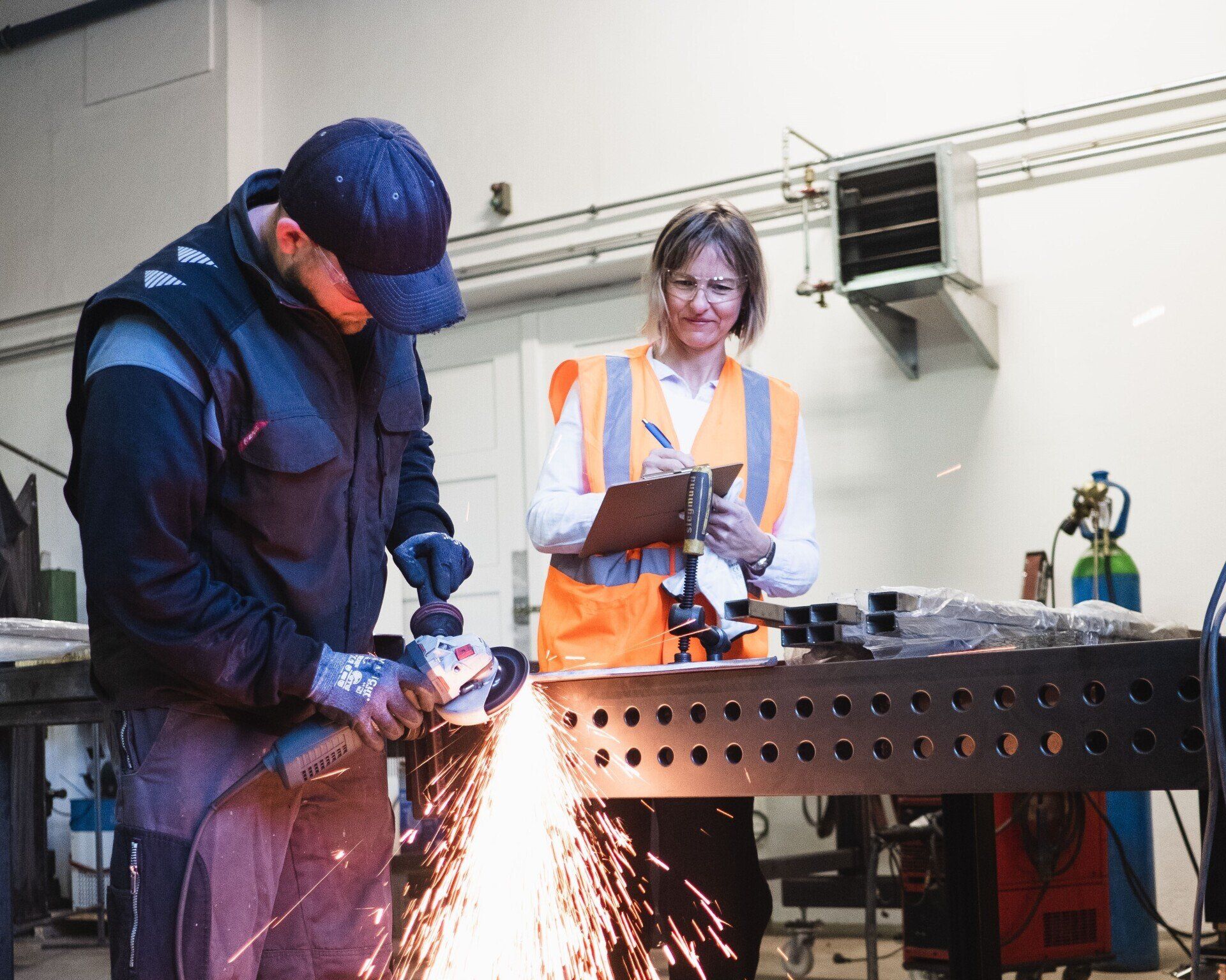 Mann, Frau, Arbeit, Kontrolle, orange Warnweste, blaue Arbeitsbekleidung, Sicherheitsfachkraft (SFK)