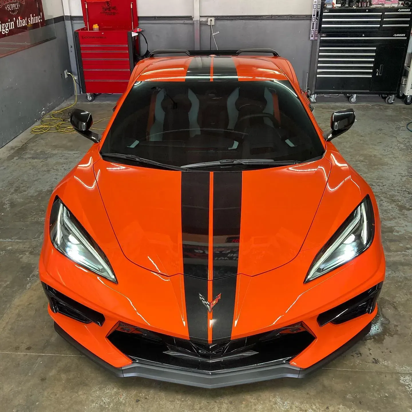 Black Chevrolet Camaro in a garage, black wheels, yellow line on the floor, promotional banners on the wall.
