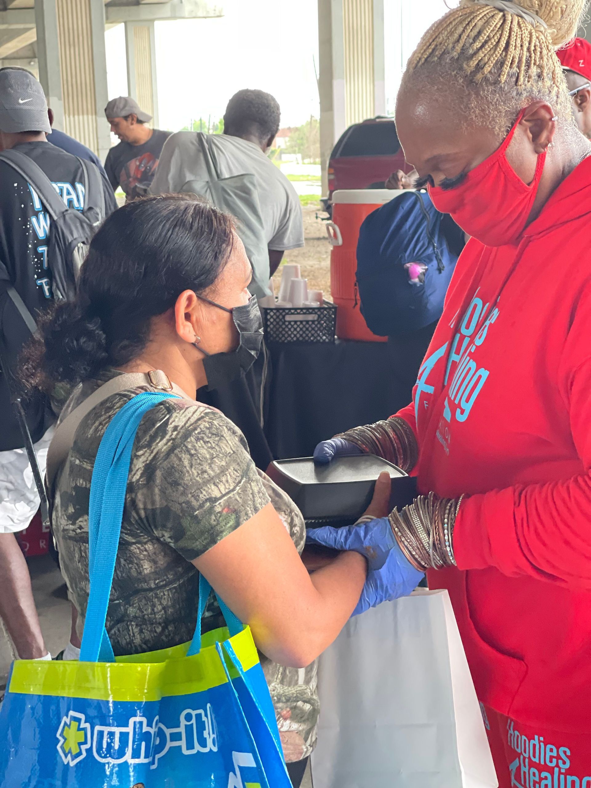 A woman wearing a red hoodie is talking to another woman wearing a mask.
