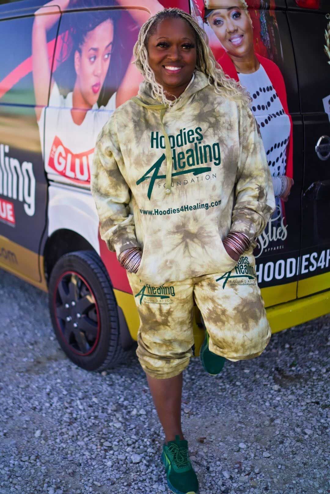A woman wearing a tie dye hoodie and shorts is standing in front of a van.