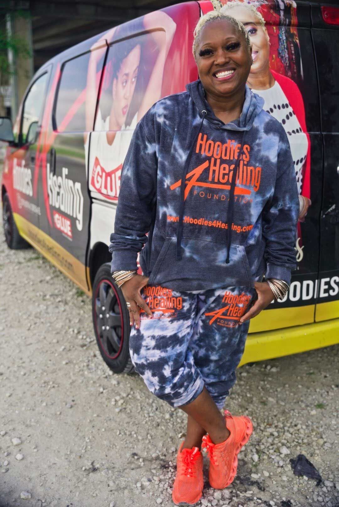 A woman in a tie dye hoodie is standing in front of a van.