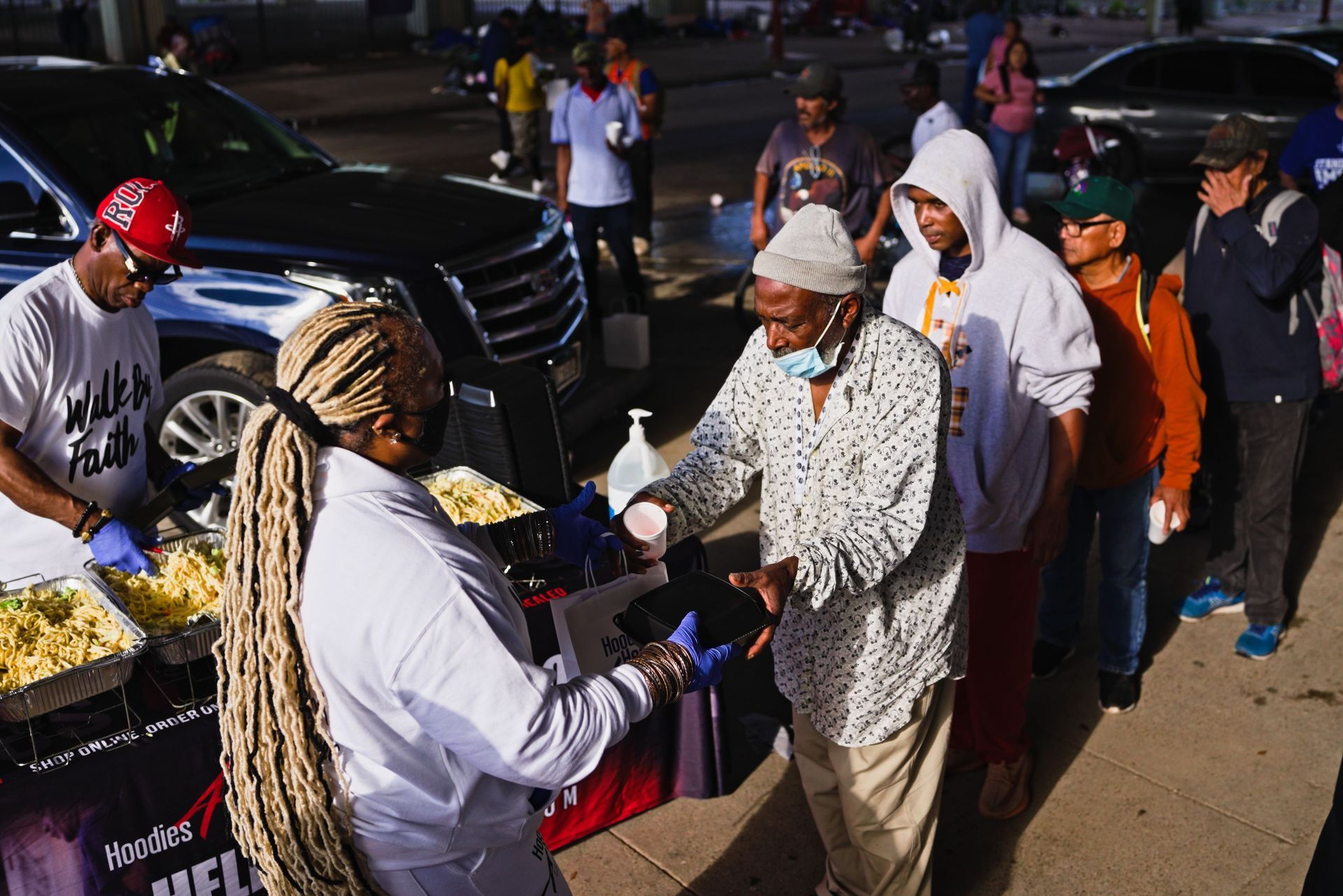 A group of people are standing in line to get food from a woman.