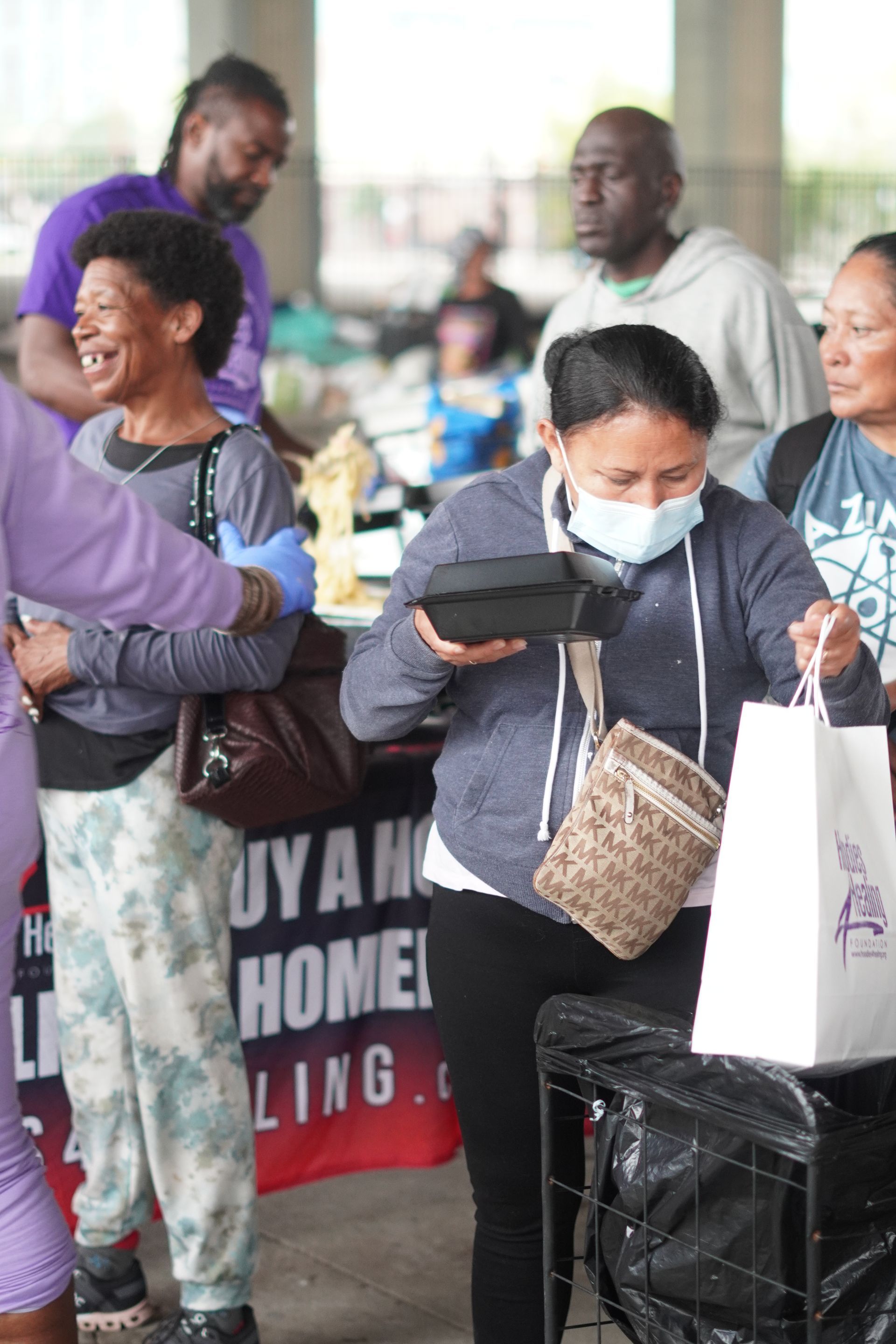 A woman wearing a mask is standing in front of a sign that says buy a home