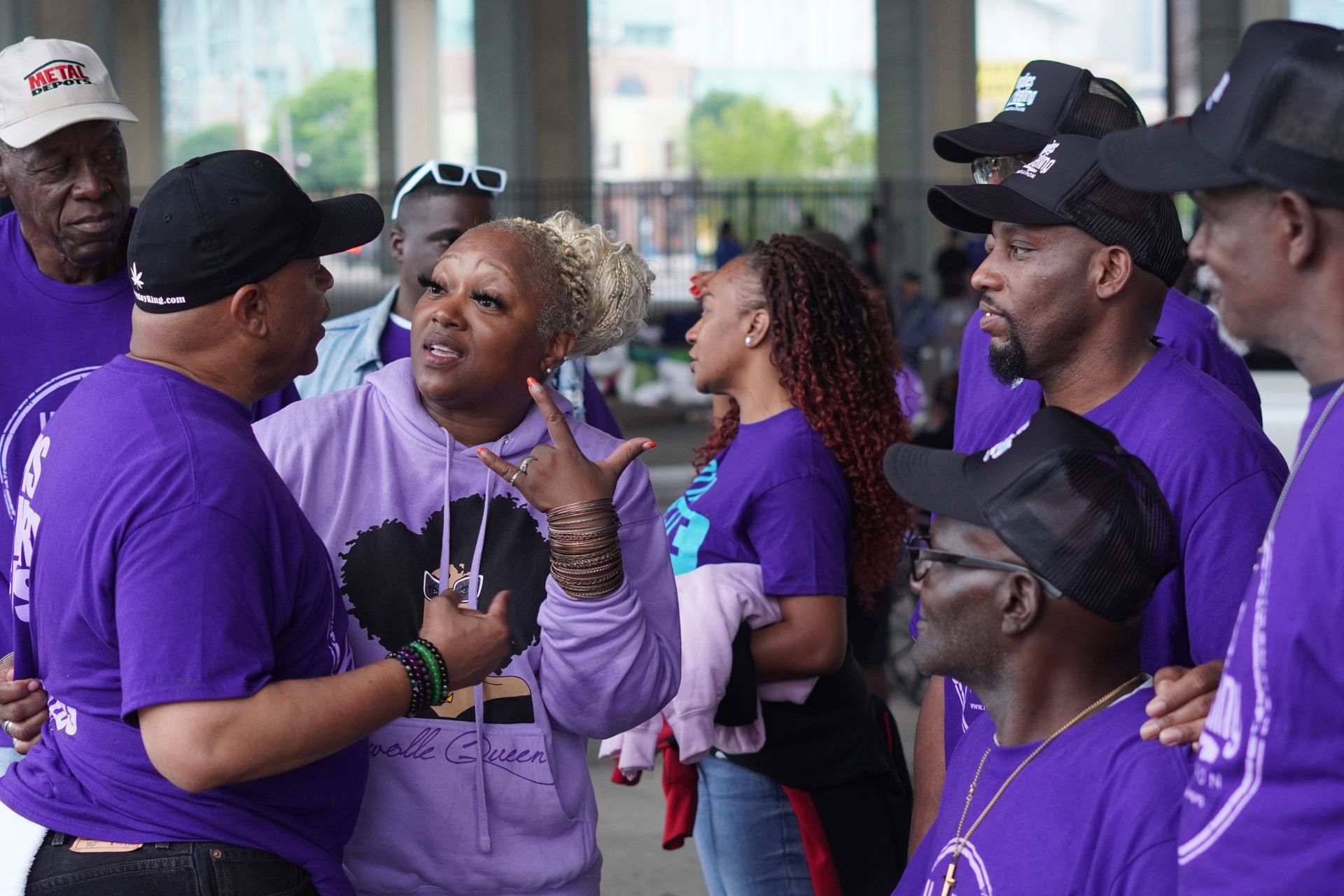 A group of people wearing purple shirts are standing around talking to each other.