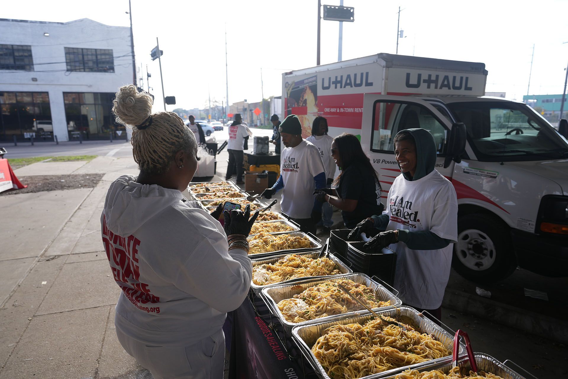 A group of people are standing around a table with food in front of a u-haul truck.