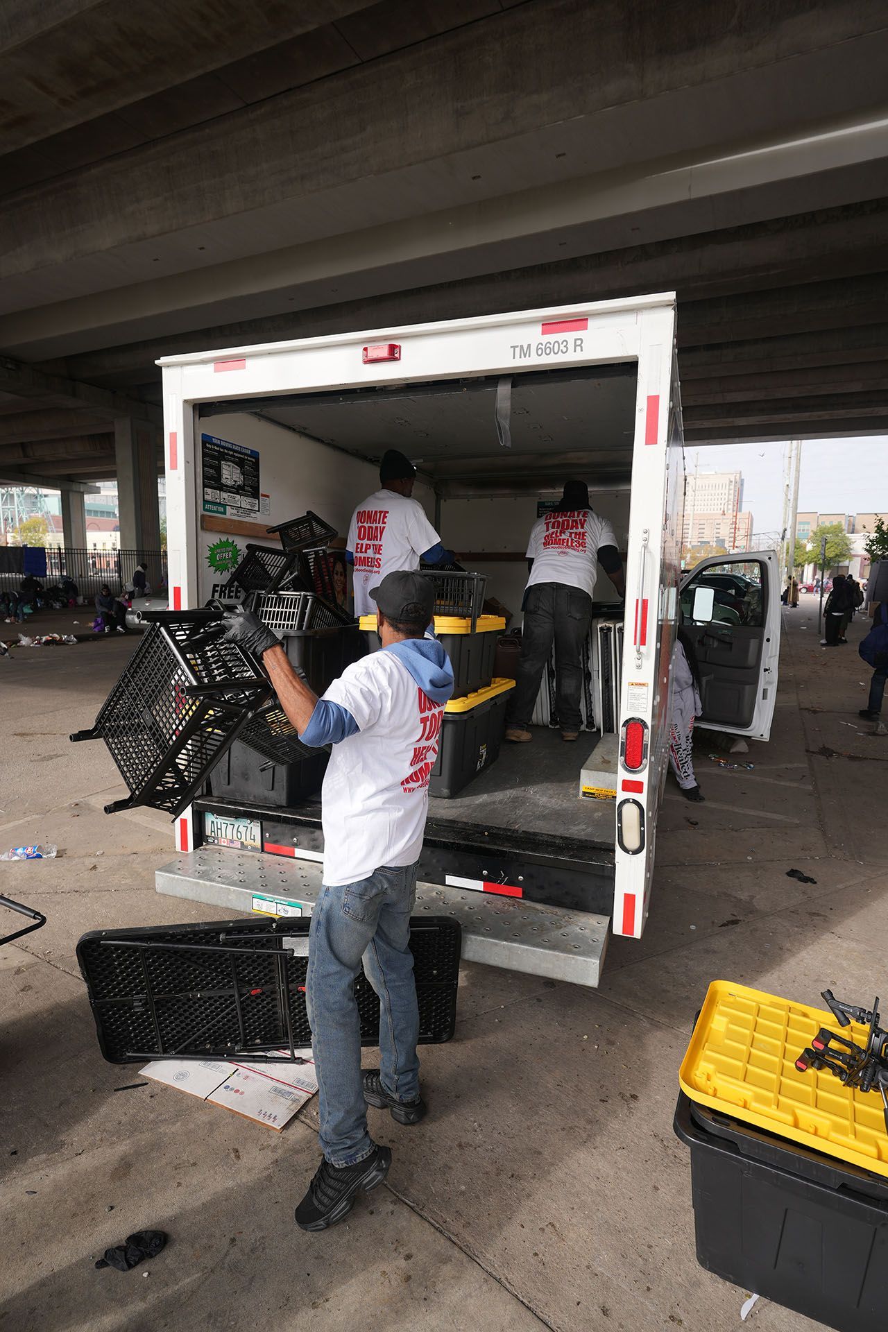 A man is loading crates into a truck under a bridge.