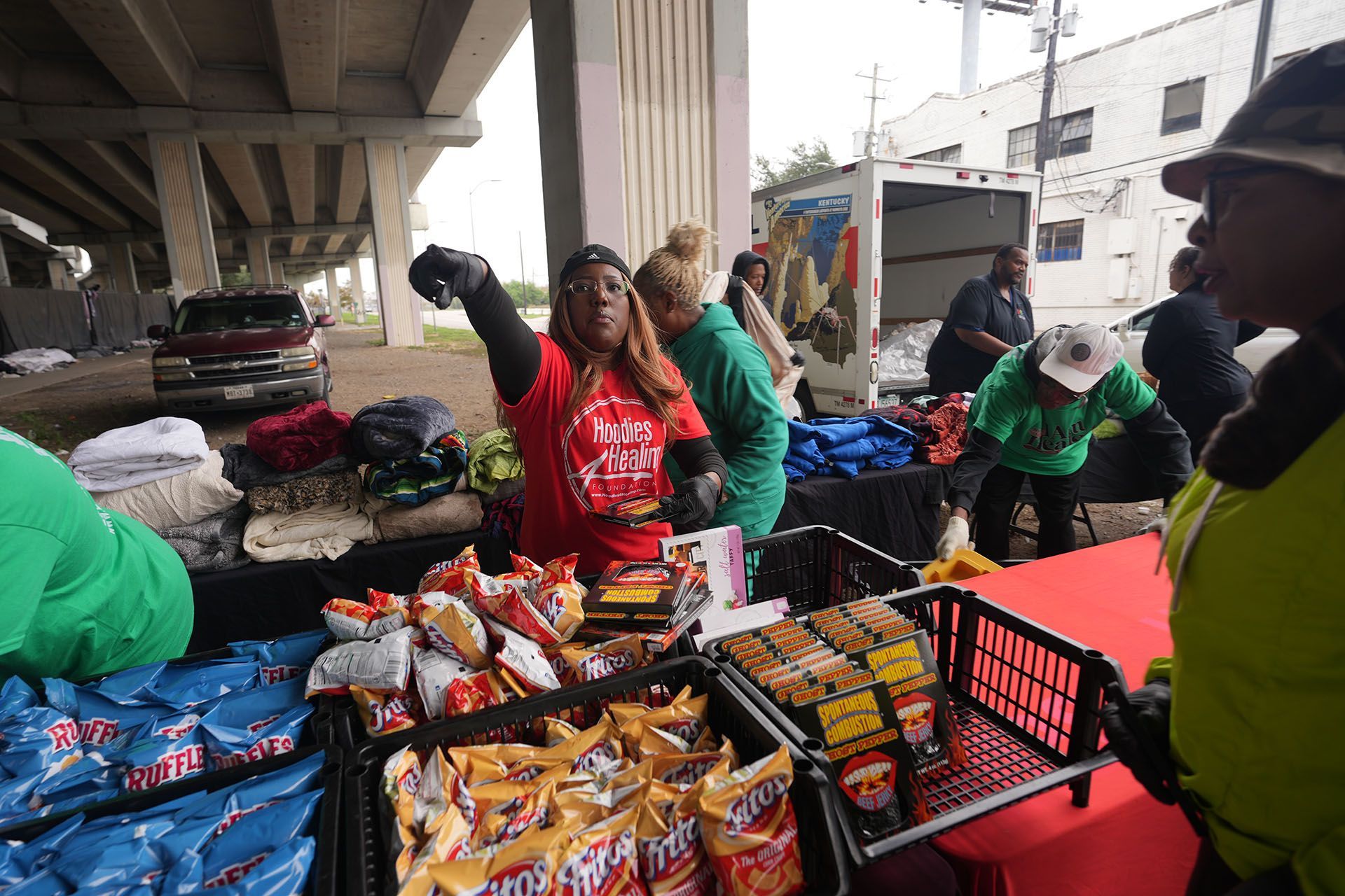 A group of people are standing around a table filled with bags of chips.