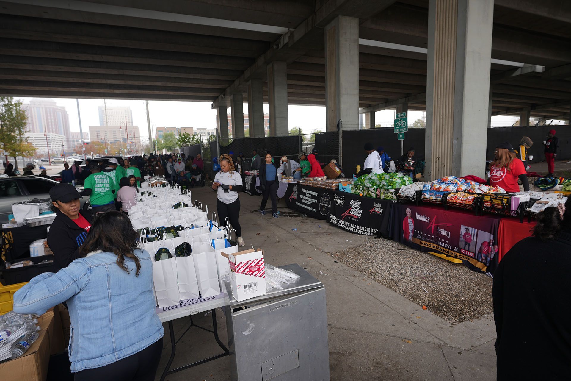 A group of people are standing around tables at a market under a bridge.