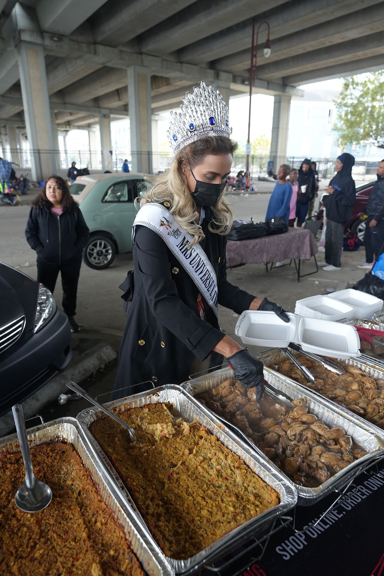 A woman in a crown is standing in front of a table with trays of food.