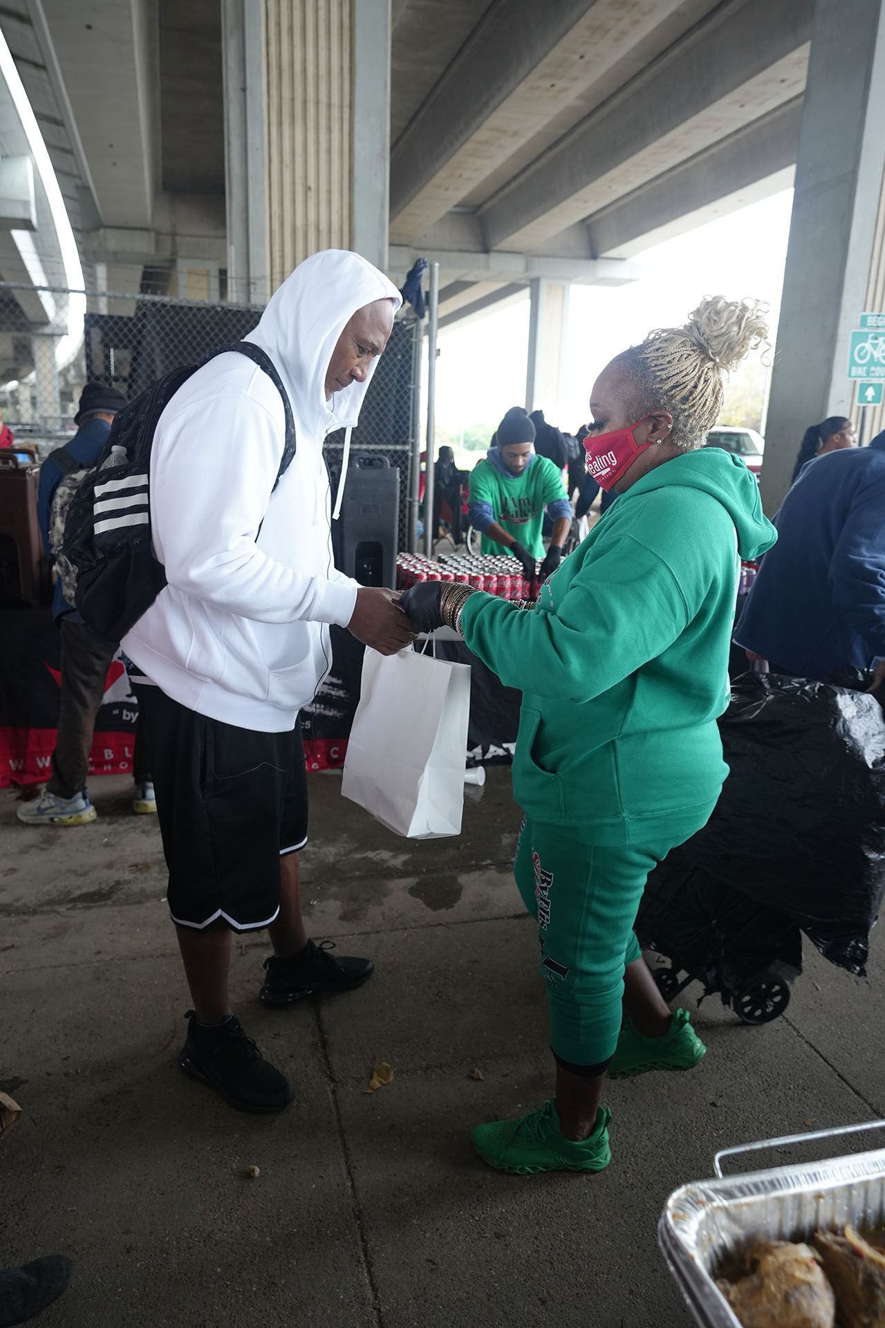 A man in a white hoodie is giving a gift to a woman in a green hoodie.