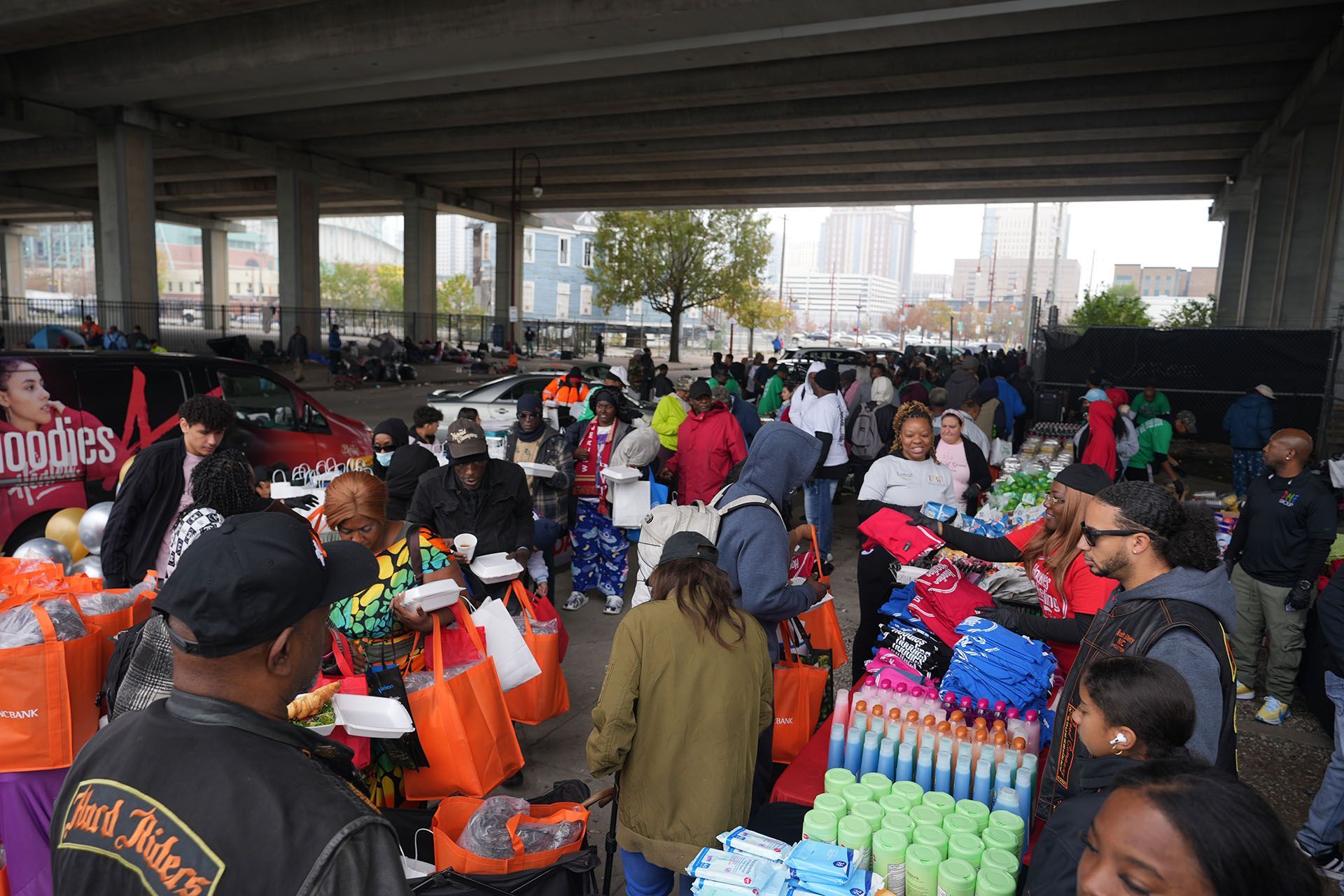 A crowd of people are gathered in a parking lot under a bridge.